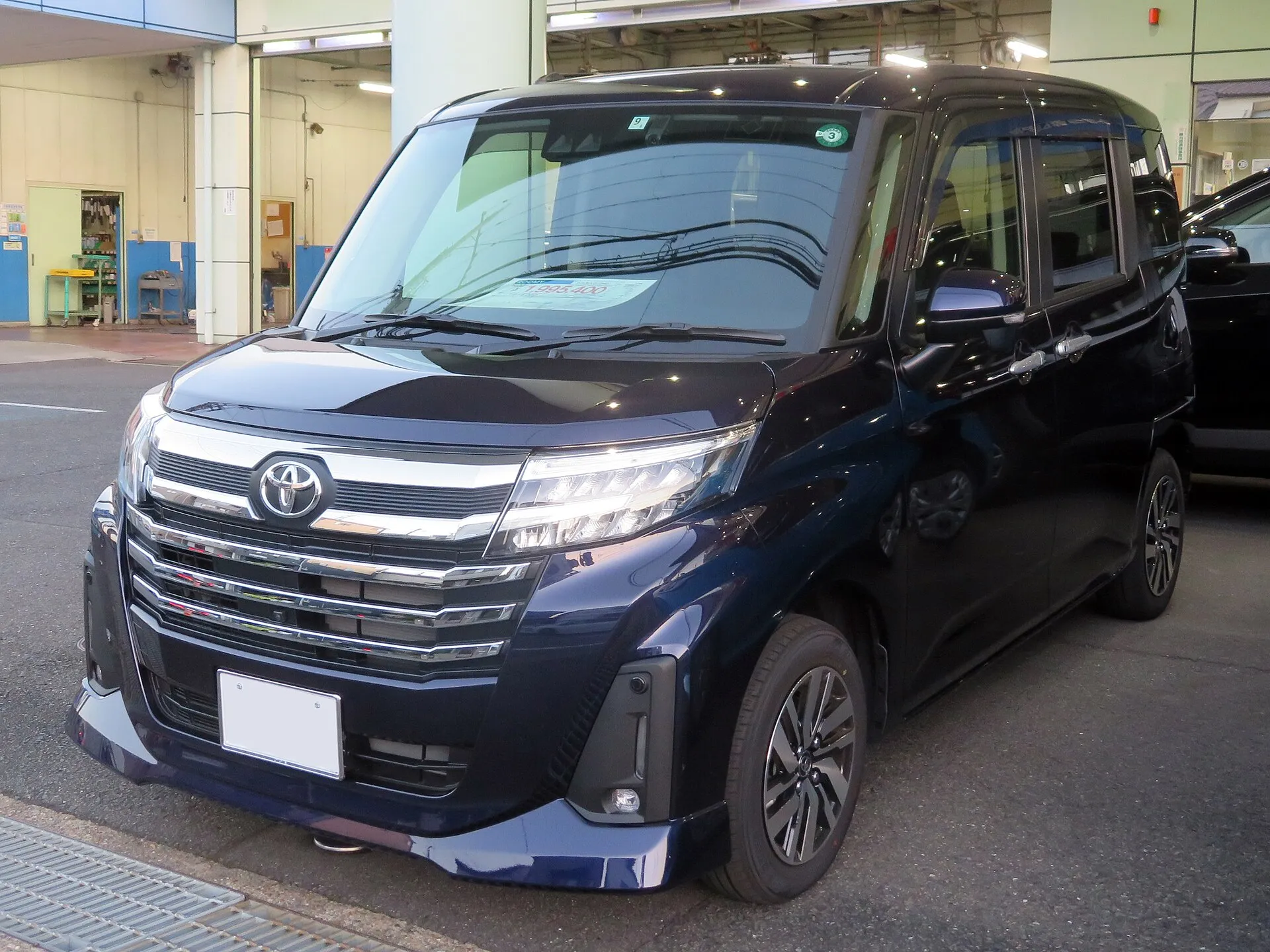 トヨタ ルーミー カスタムG 2WD（5BA-M900A-GBVE）の、2026年8月の一部改良より前の個体を前方から見た外観。濃紺のボディに、メッキの横桟が並ぶフロントグリルと14インチアルミホイールが見える