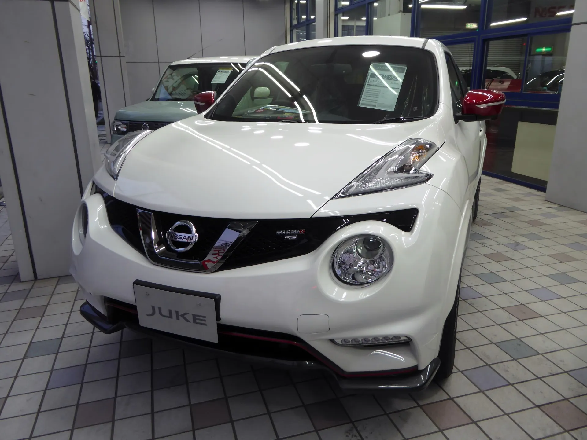 白い日産 ジューク NISMO RS（F15型）を正面やや左から見た外観。前後バンパー下端に赤いラインが入る