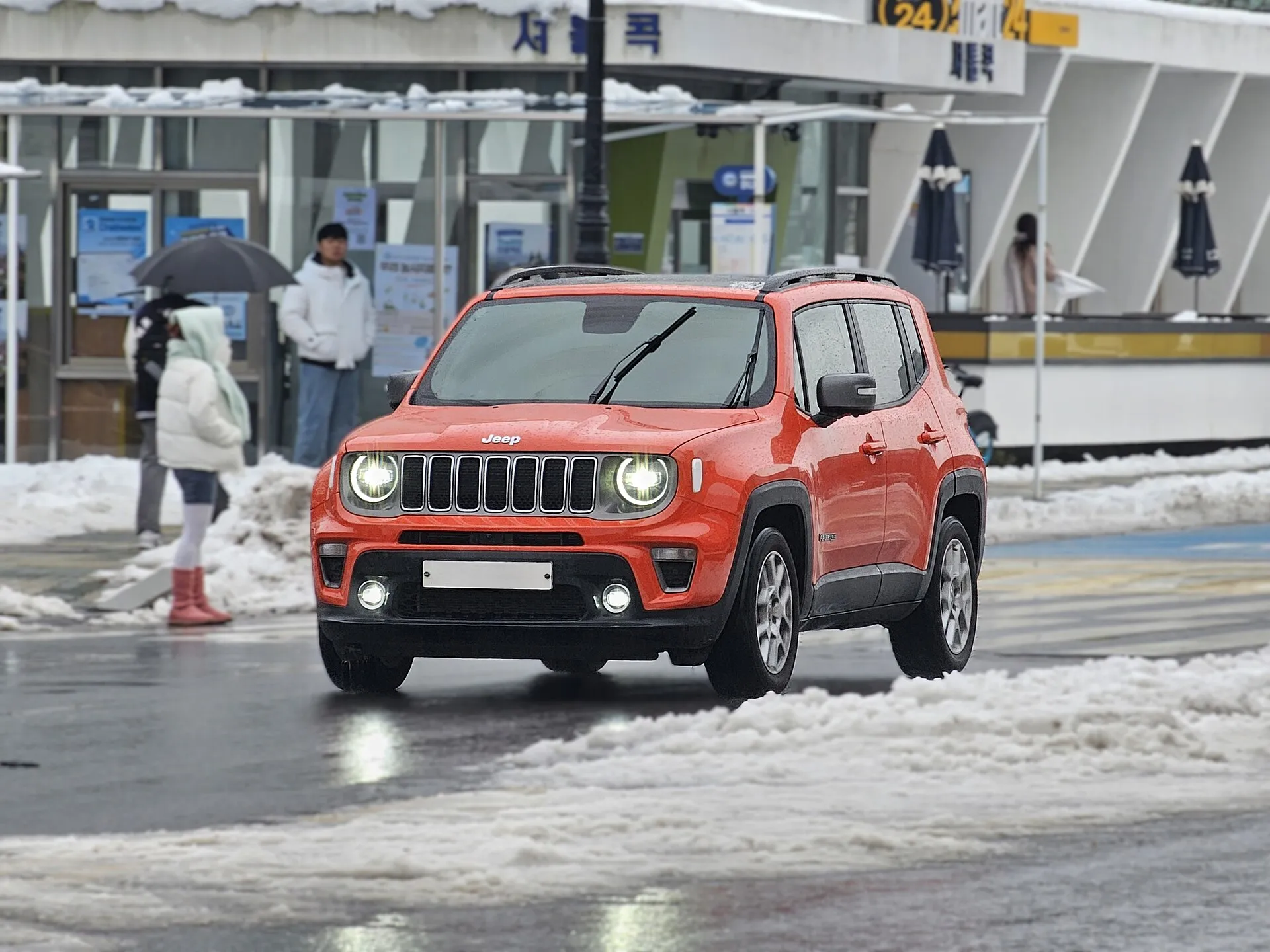 雪の残る路面を走るジープ レネゲード（フェイスリフト後）を正面から見たところ。7スロットグリルとヘッドライトが点灯している