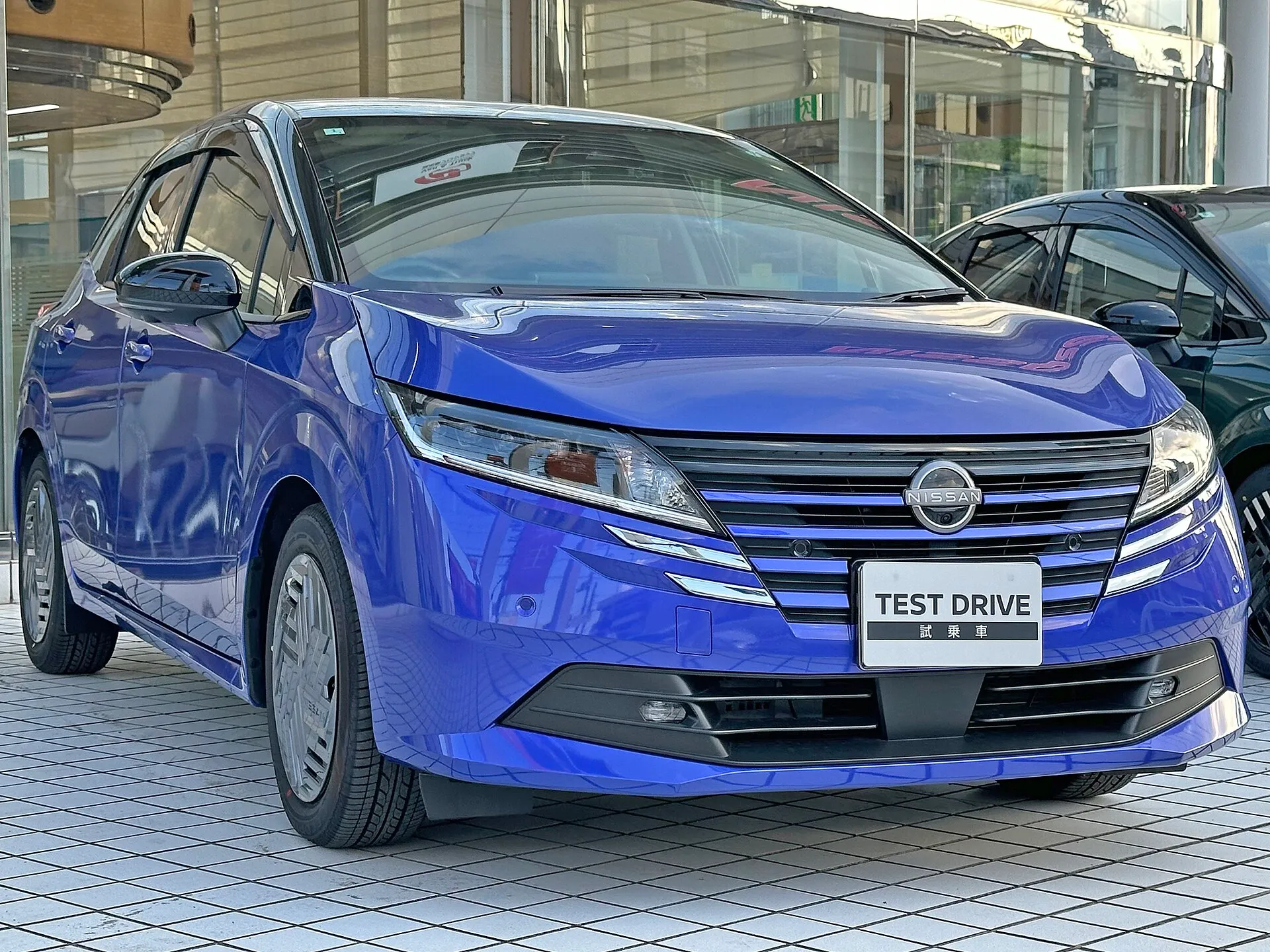 日産 ノート X（6AA-E13）を右前方から見た外観。青いボディに16インチフルホイールカバー
