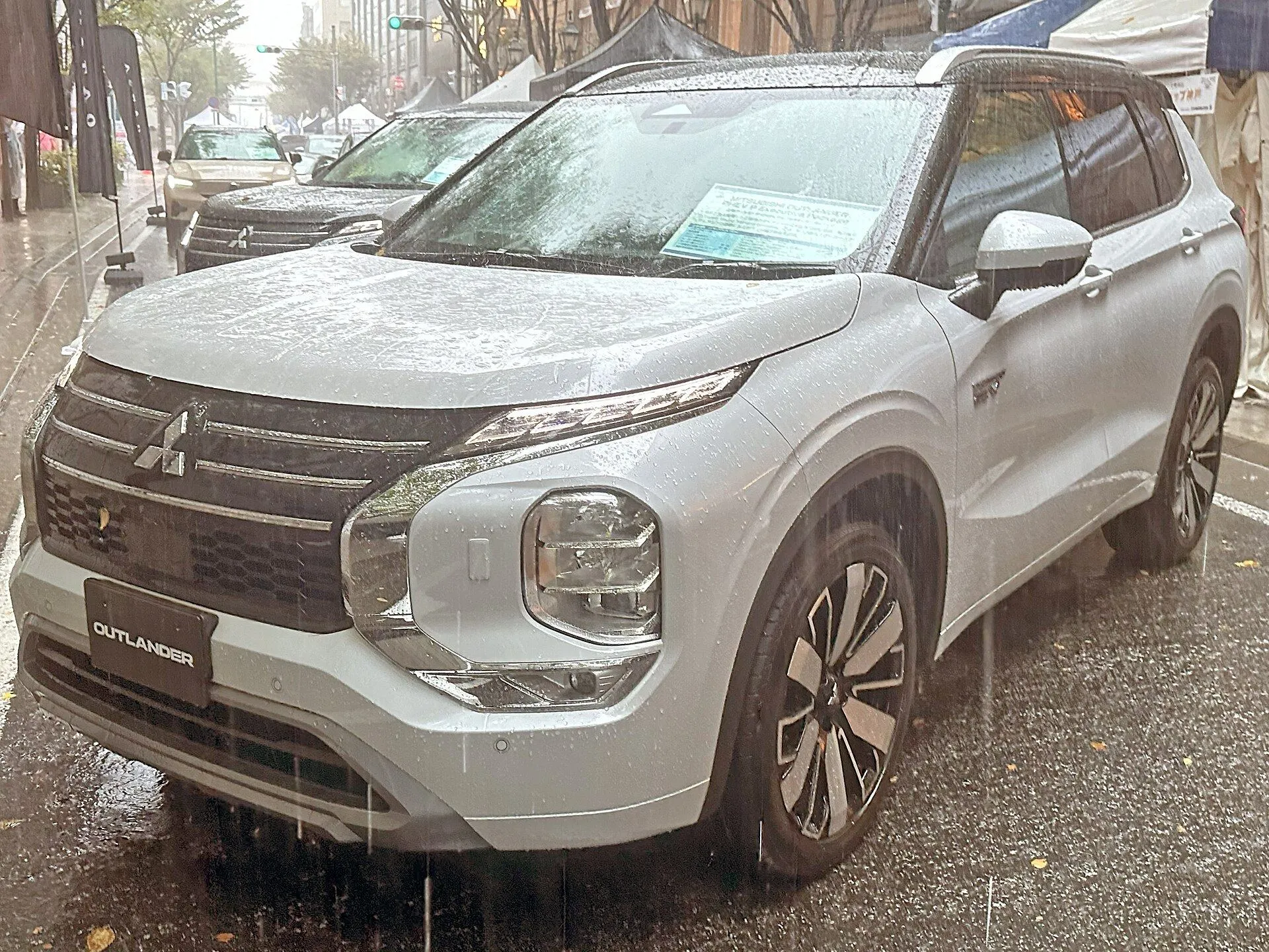 白い三菱 アウトランダーPHEV P Executive Package（5LA-GN0W）を斜め前から見た外観。クロームのフロントグリルモールディングとボディ同色のドアミラーが見える