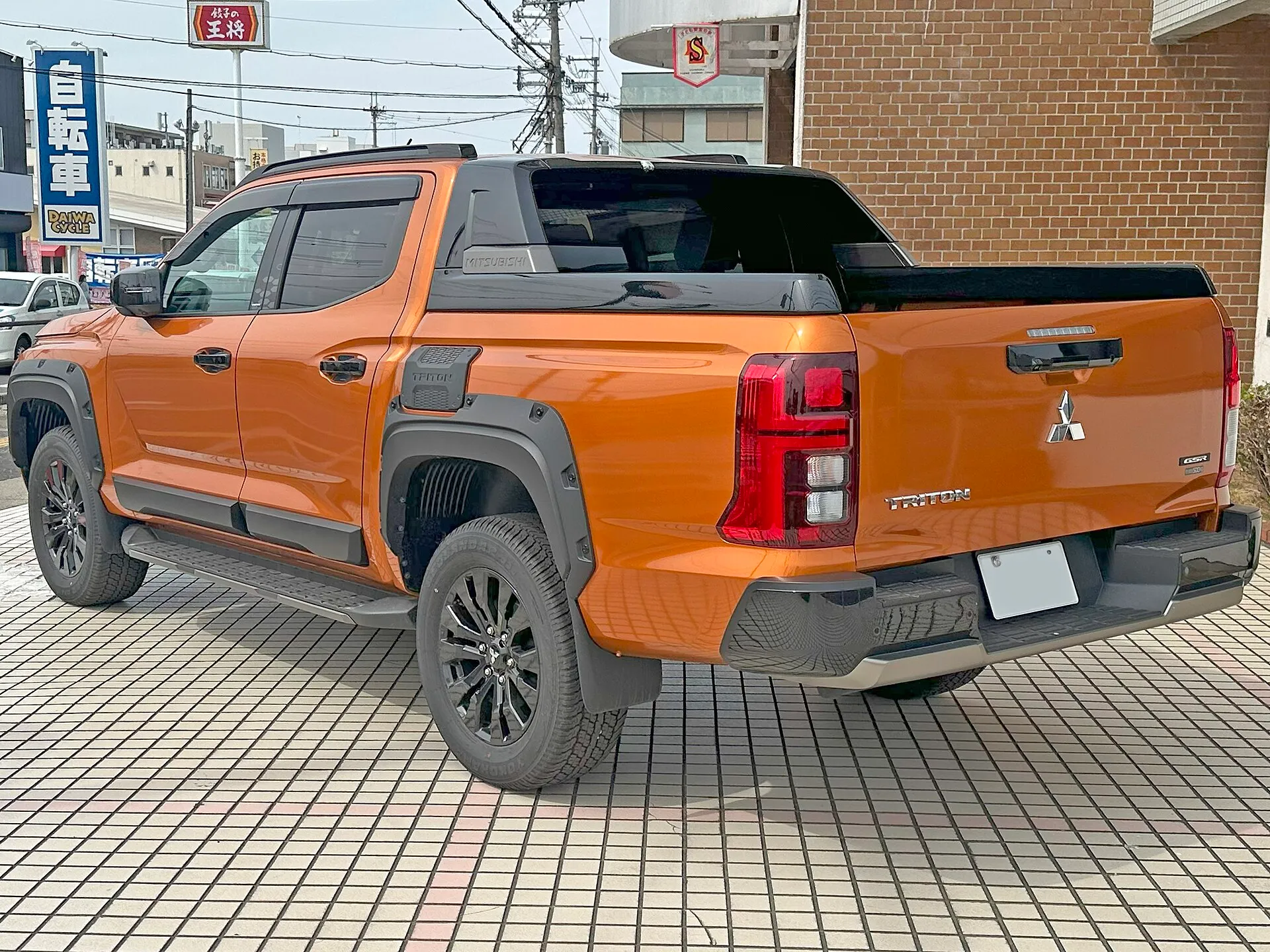 オレンジのトライトン GSR を左後方から見た外観。荷台の前端に黒いスタイリングバーが立ち、GSRバッジとリヤゲートハンドルが見える