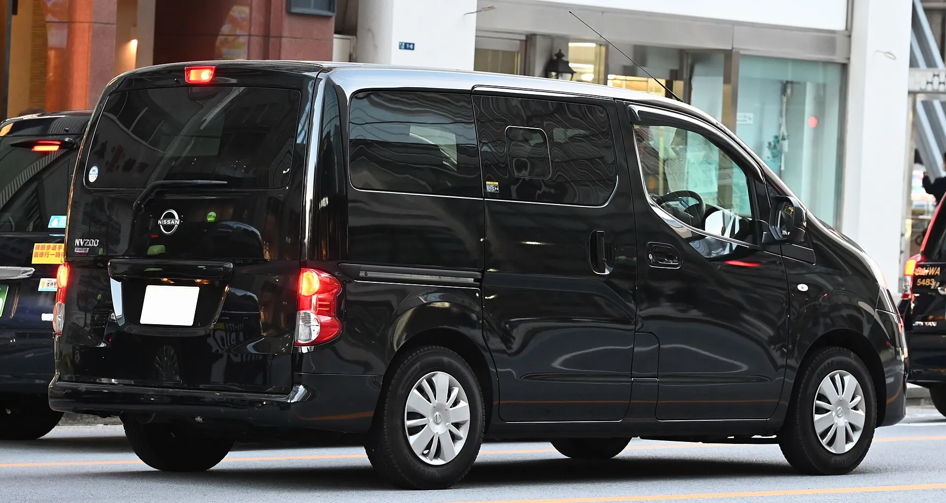 日産 NV200バネット ワゴン 16X（マルチベッドの架装がない車両）を斜め後ろから見た外観。黒い車体