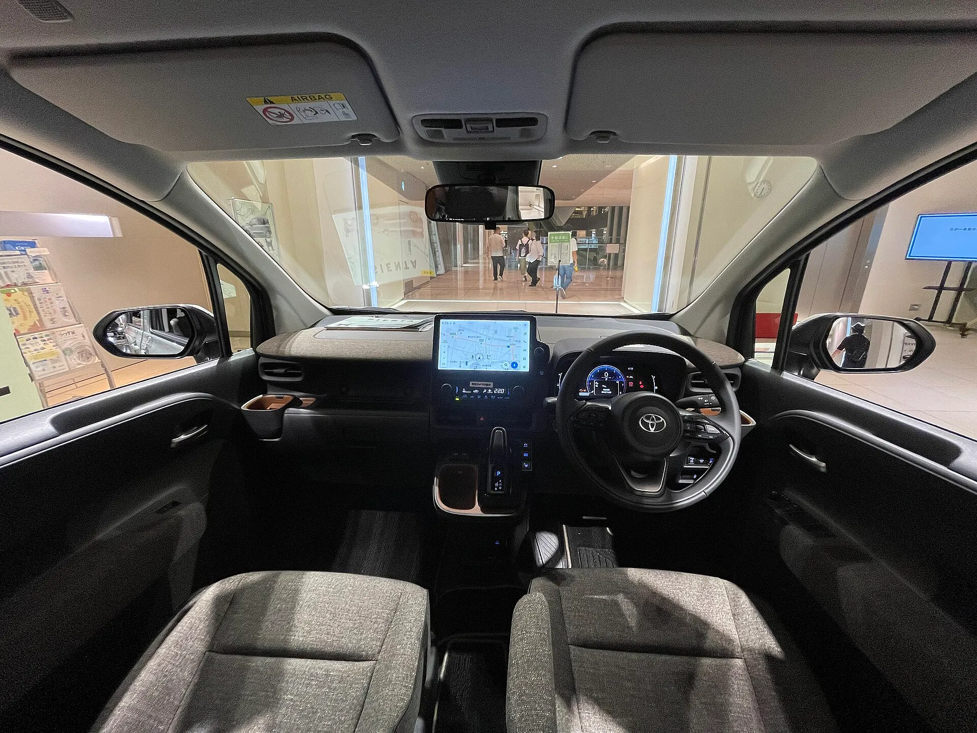 シエンタ HYBRID Z(2WD・7人乗り)の前席まわりを後席側から見た様子。ダッシュボード中央にディスプレイ、運転席の前にデジタルメーター、グレーのファブリックシートが見える
