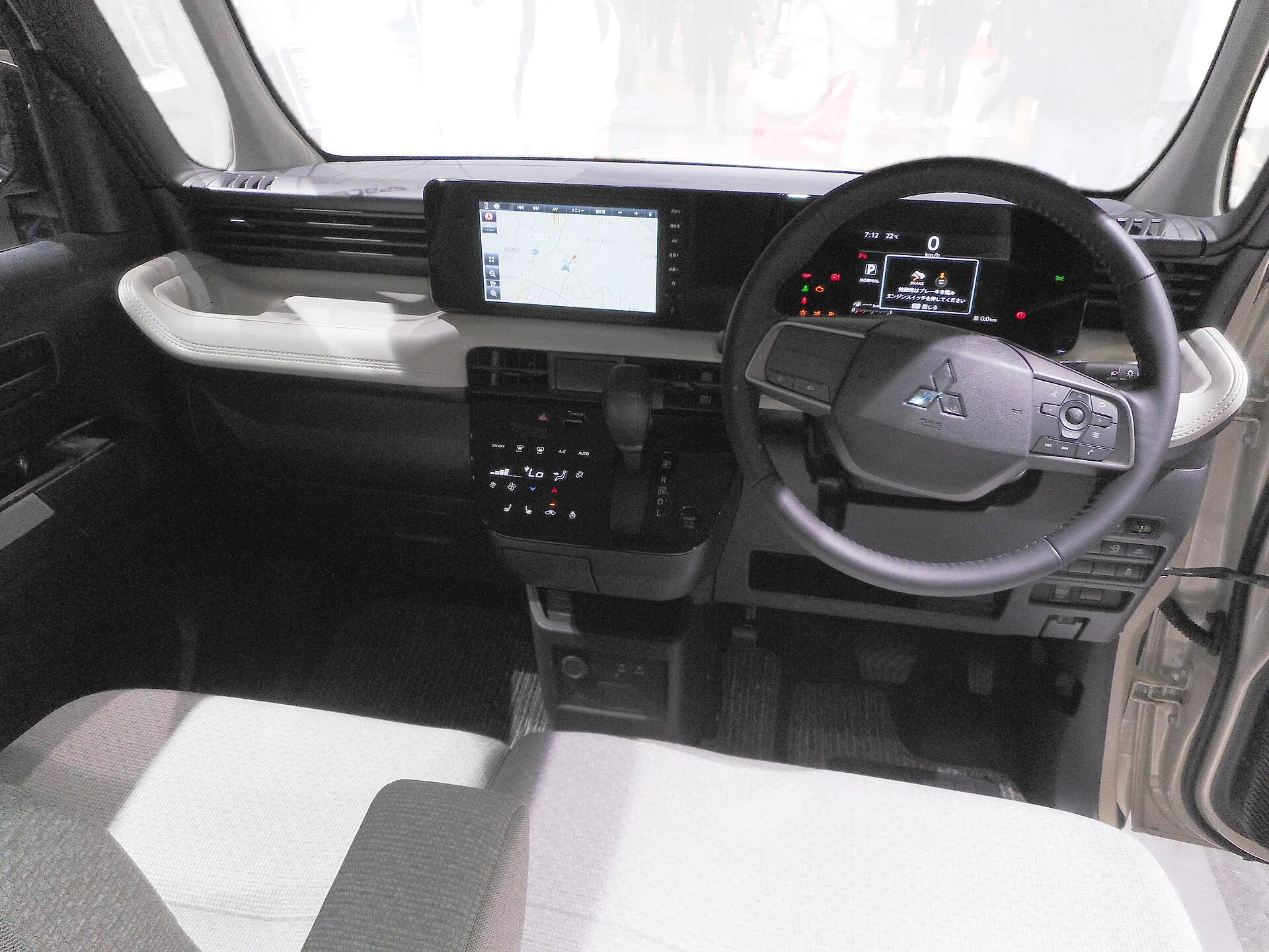 三菱 eKスペース G の運転席まわりを後ろから見た様子。ダッシュボード中央にナビゲーションの画面、ステアリングの奥にメーター、手前にグレーのファブリックのシートが見える