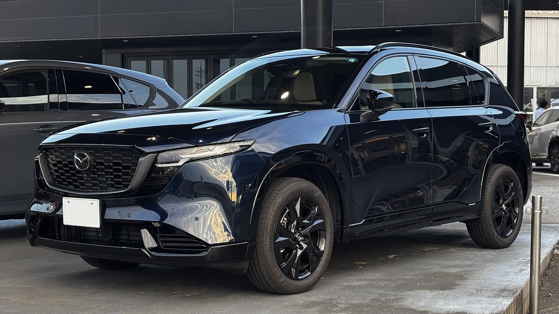 濃い青のマツダ CX-5 L を左前方から見た外観。黒いアルミホイールを履き、バンパーの下側とフェンダーまわりが黒い