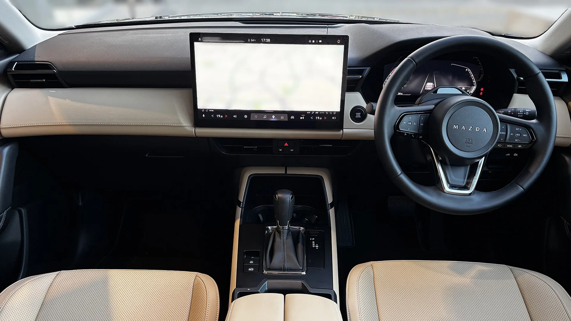 CX-5 L の前席まわりを後席側から見た様子。ベージュ系の色のシートと、ダッシュボードの横長の加飾、中央の大きな画面が見える