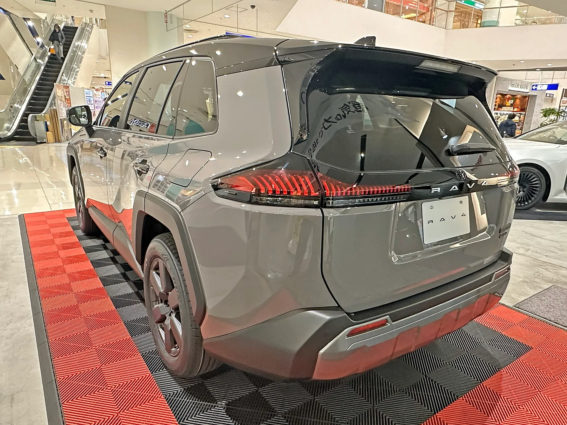 グレーのトヨタ RAV4 Adventureを左後方から見た外観。黒いルーフとバックドアの上部、赤いテールランプ、濃いグレーのアルミホイールが見える、型式6AA-AXAN64-ANXVBの個体