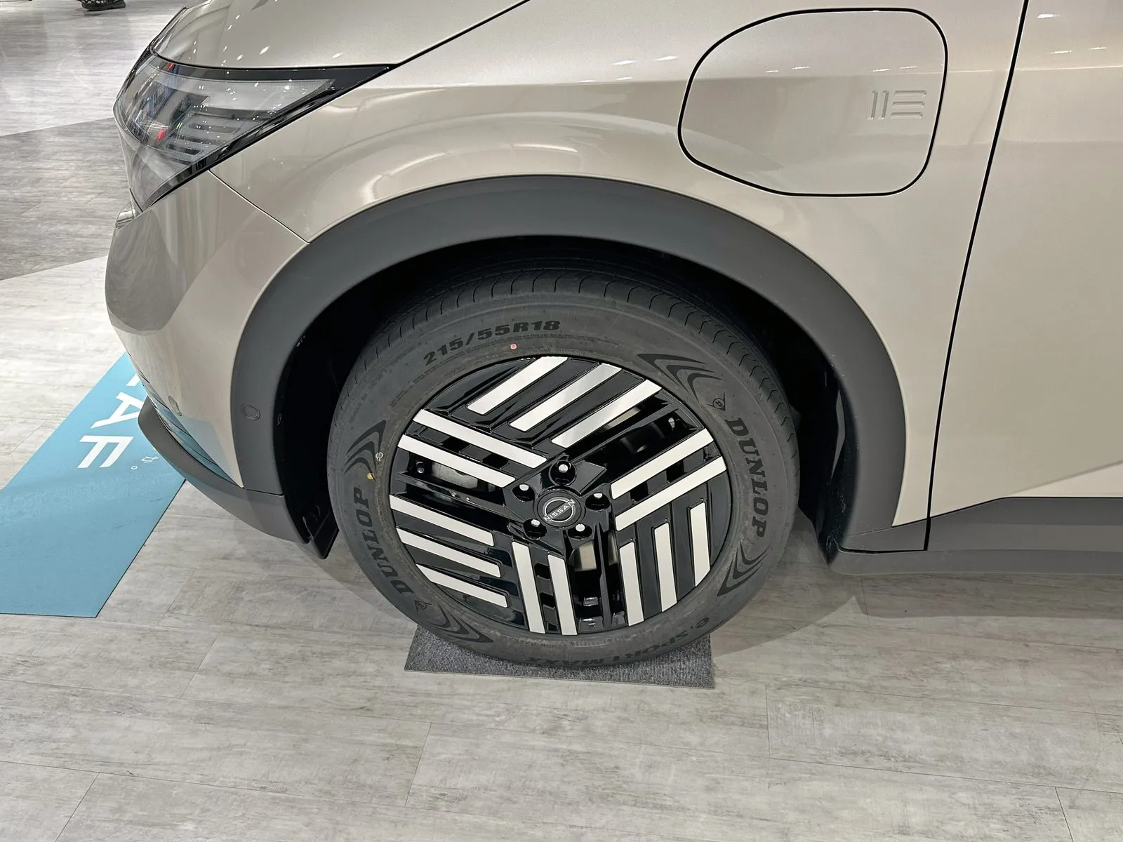 日産 リーフ B7 X（ZAA-ZE2）の左前輪まわりの接写。タイヤのサイドウォールに「215/55R18」の刻印が見え、黒地に白いスポークの18インチアルミホイールが付く