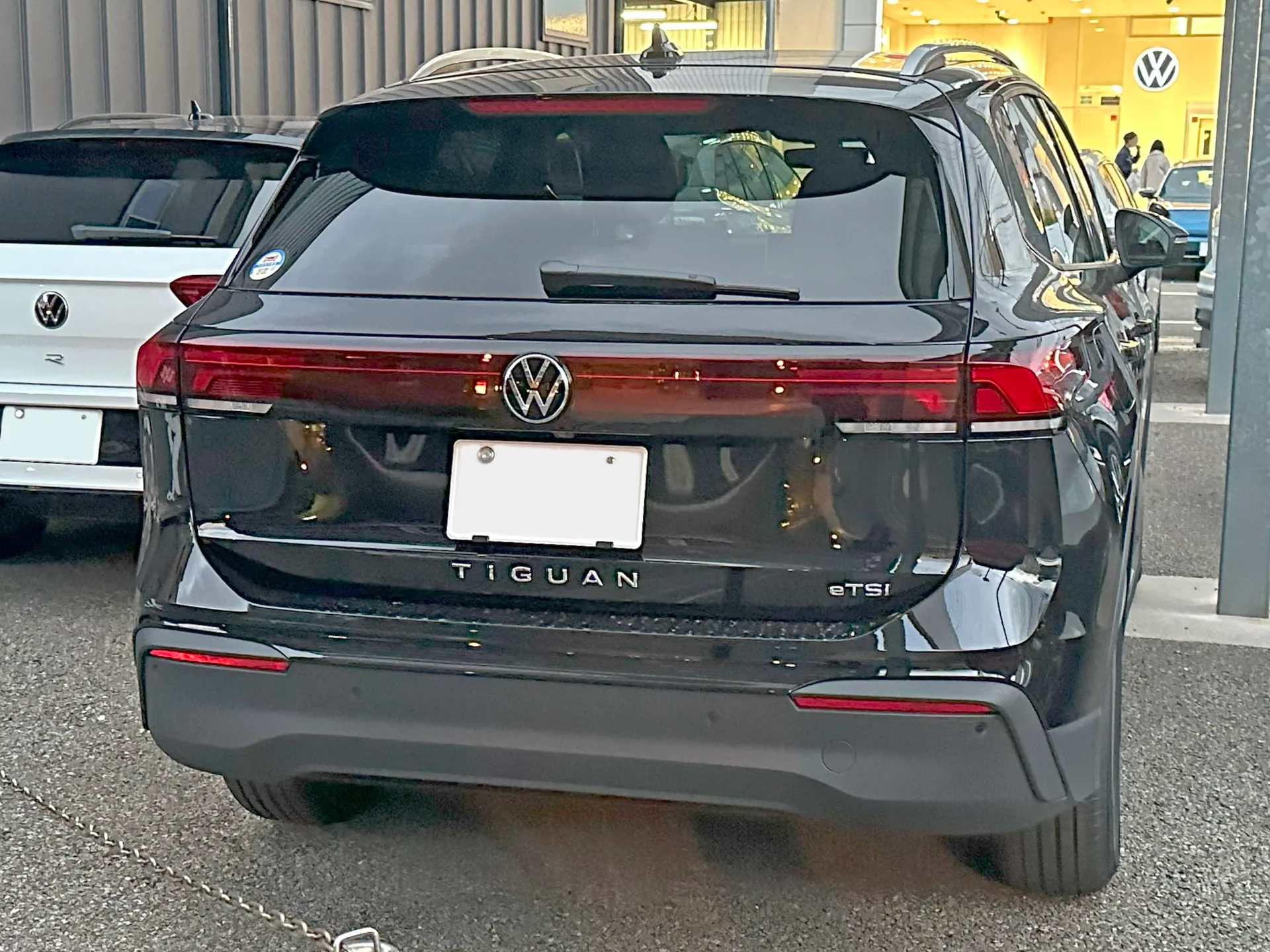 黒いフォルクスワーゲン ティグアン eTSI Active(型式3AA-CT15)を真後ろから見た外観。テールゲートに TIGUAN と eTSI のエンブレムが並び、横一文字につながるテールランプが点灯している
