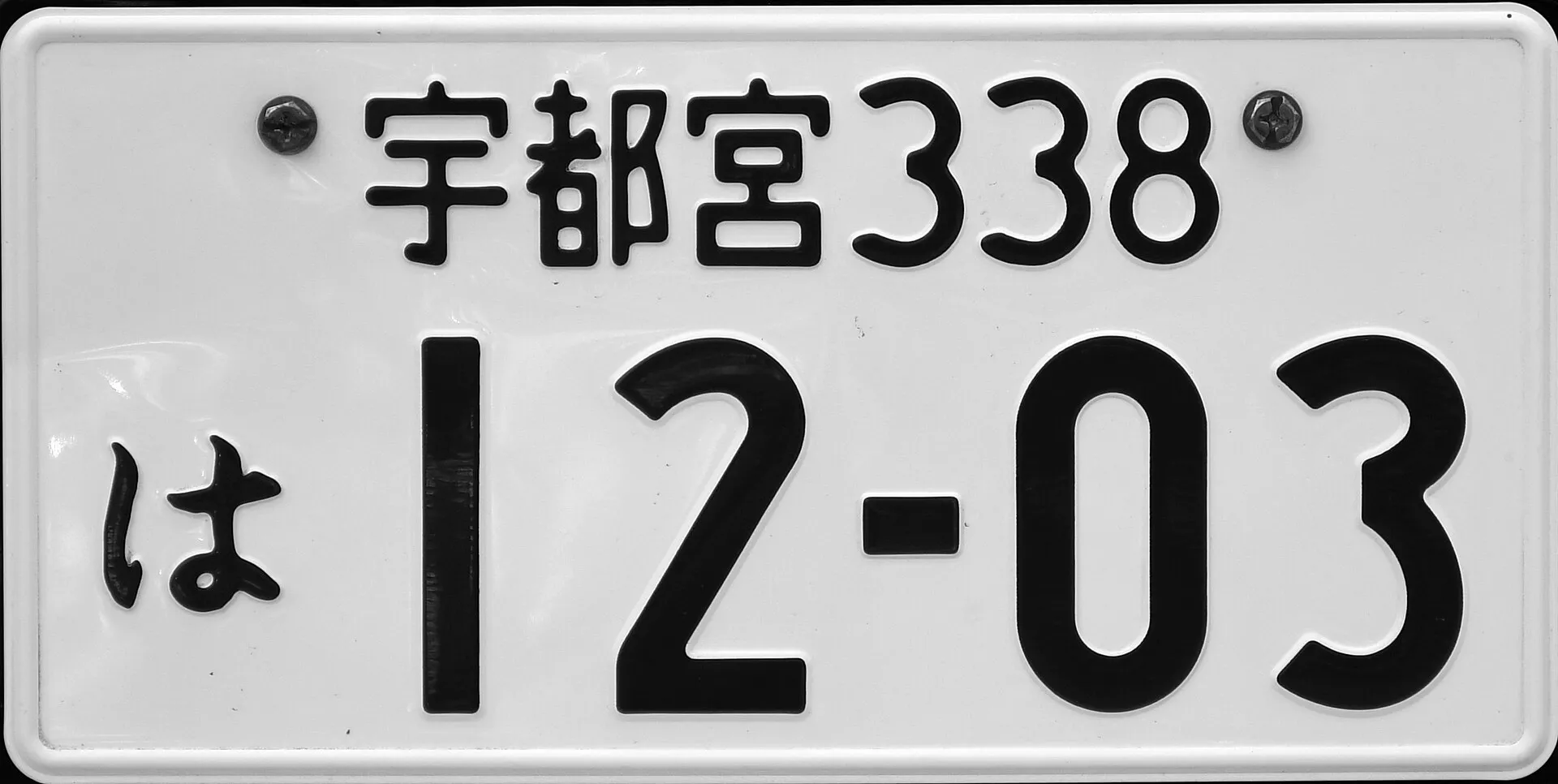 白地に黒い文字のナンバープレートを正面から写した写真。Wikimedia Commons の説明では、排気量660cm3以上の自家用車のものとされている