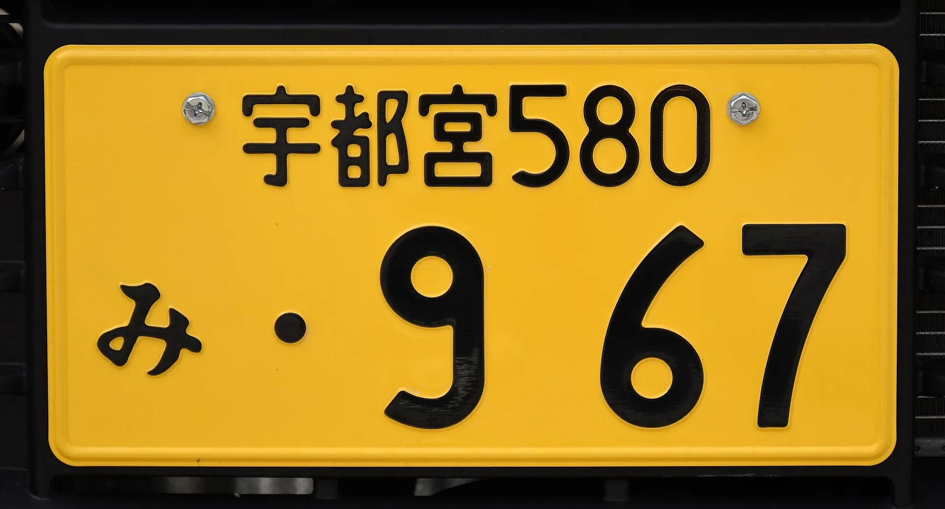 黄色地に黒い文字のナンバープレートを正面から写した写真。Wikimedia Commons の説明では、排気量660cm3未満の自家用車のものとされている
