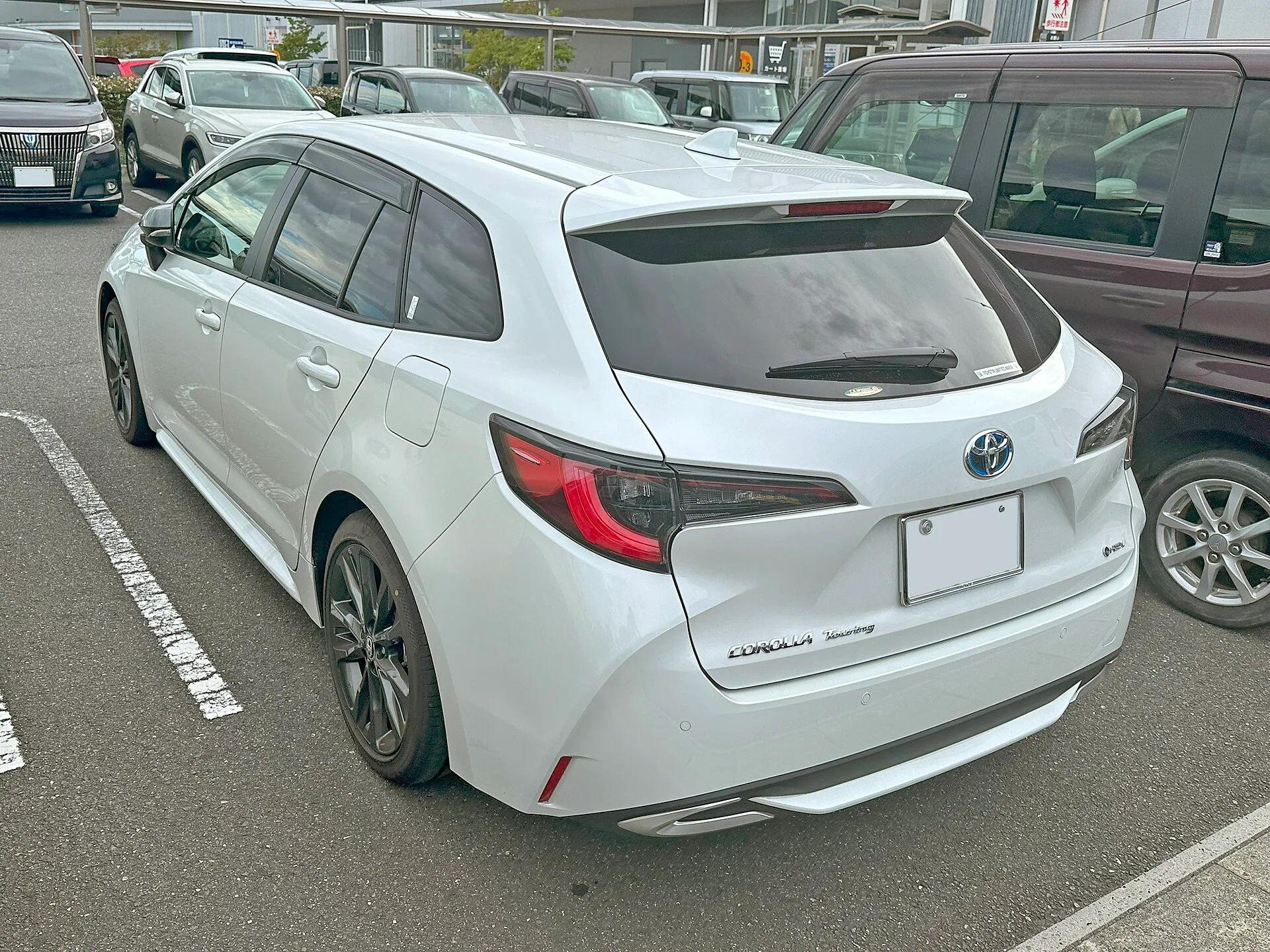 白いトヨタ カローラ ツーリング W×B（ハイブリッド）を左後ろから見た外観。リヤウインドゥにワイパーが付き、ライトガイド付のLEDリヤコンビネーションランプとリヤスポイラーが見える