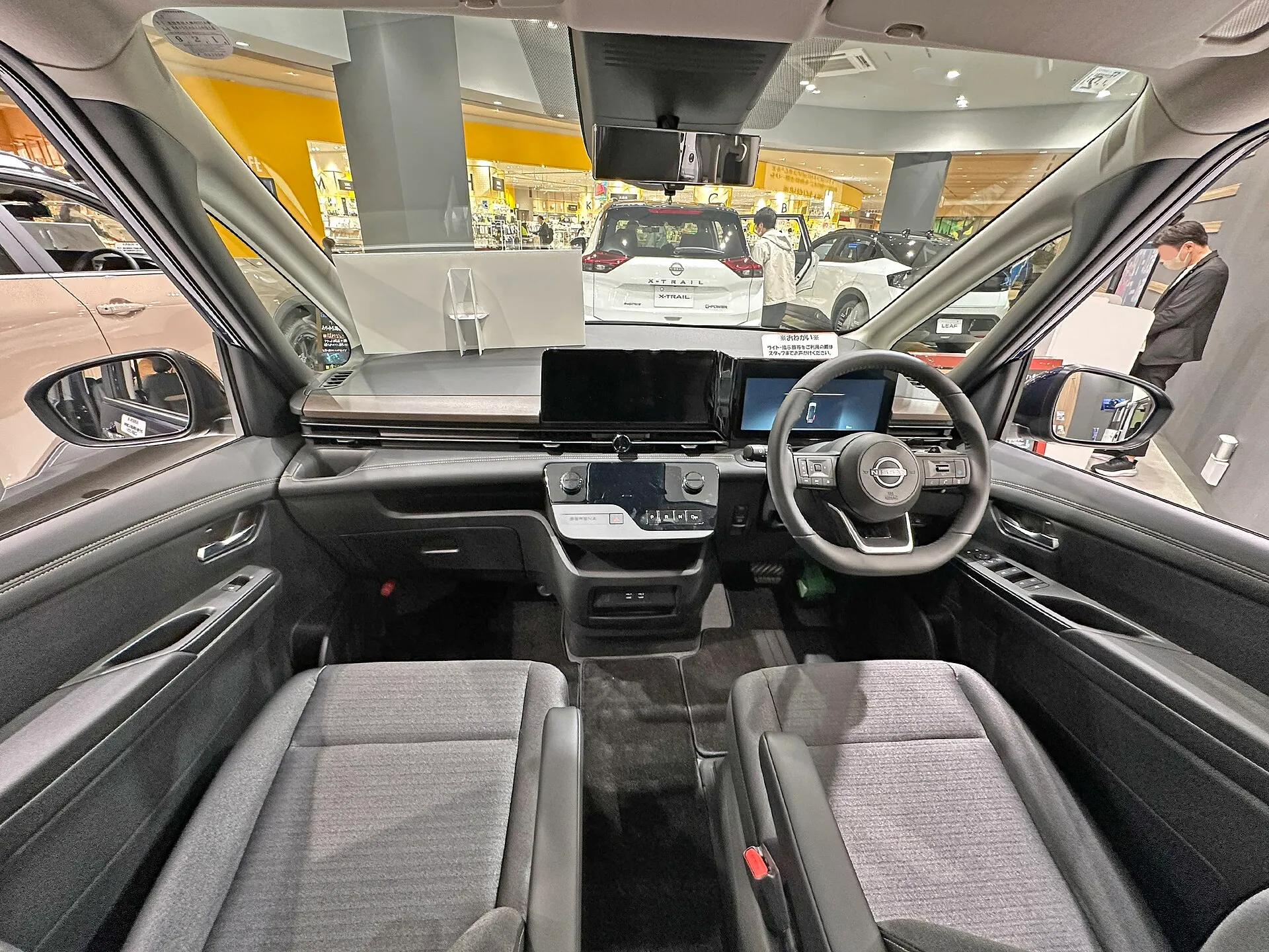 日産 セレナ e-POWER ハイウェイスターV（6AA-GFC28）の運転席まわりを後席側から見た内装。グレーの織物調の前席が左右に並び、センターコンソールのない広い足元が見える