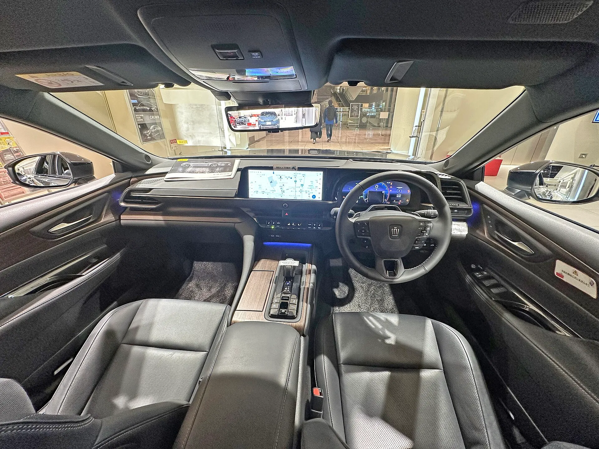トヨタ クラウン（セダン）Z（ハイブリッド車・6AA-AZSH32-CEVGB）の、改良前の個体の前席まわりを後席から見た様子。黒い革のシートの間にセンターコンソールがあり、その先に横長の画面とステアリングホイールが見える