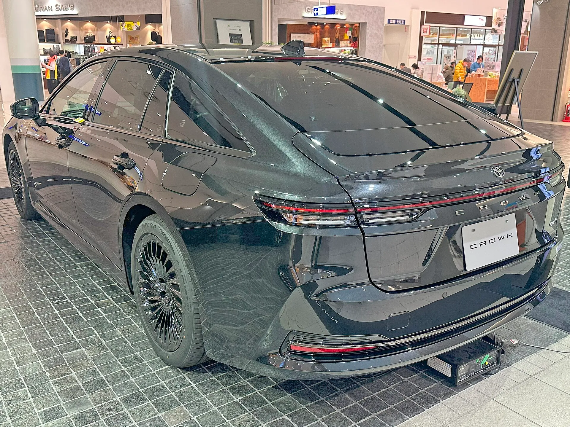 トヨタ クラウン（セダン）Z（ハイブリッド車・6AA-AZSH32-CEVGB）の、改良前の個体を左後方から見た外観。濃い色のボディと黒い多スポークのアルミホイール、横一文字につながるリヤコンビネーションランプが見える