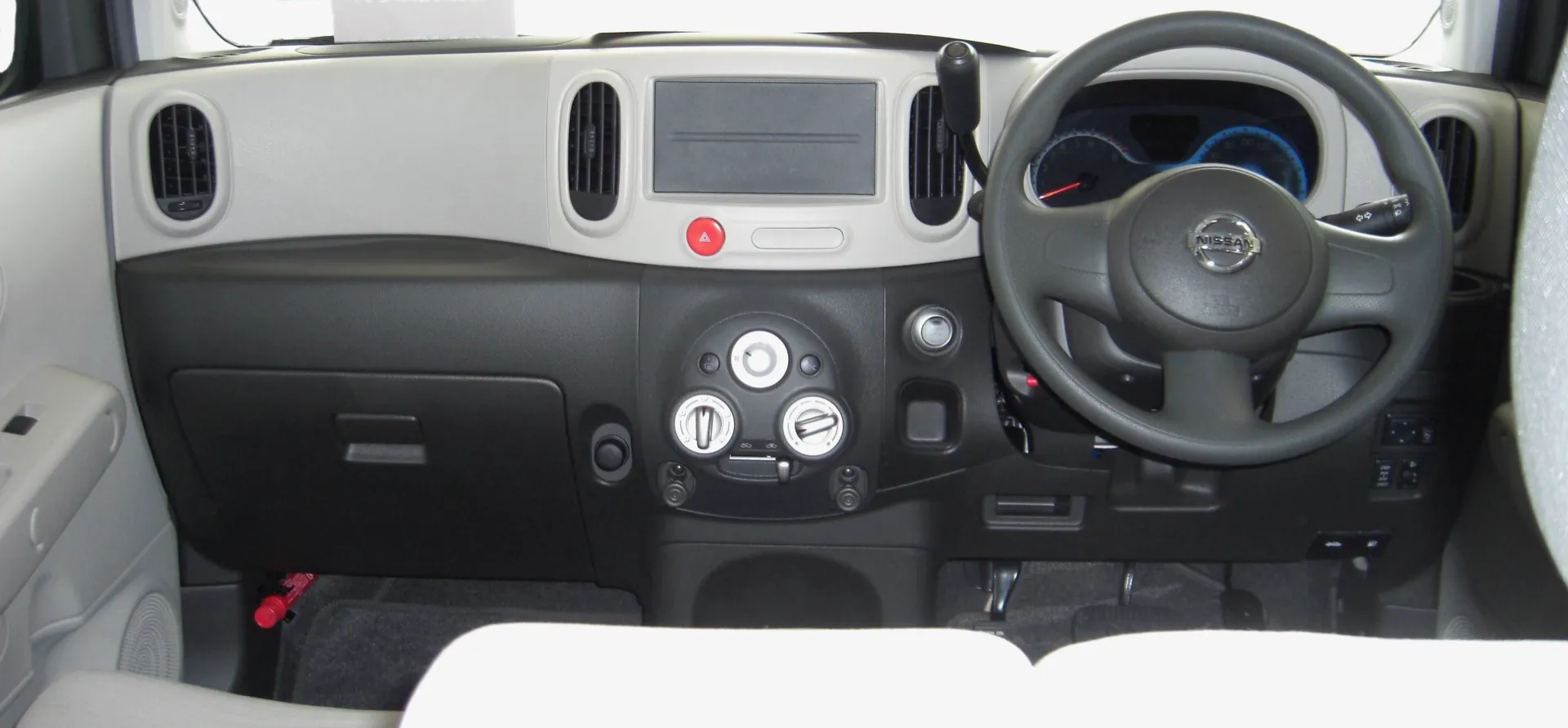 日産 キューブ（Z12）の運転席まわりを助手席側から見た様子。ダッシュボード中央の下に丸いダイヤル式のエアコン操作部が並び、右ハンドルのステアリングとメーターが見える
