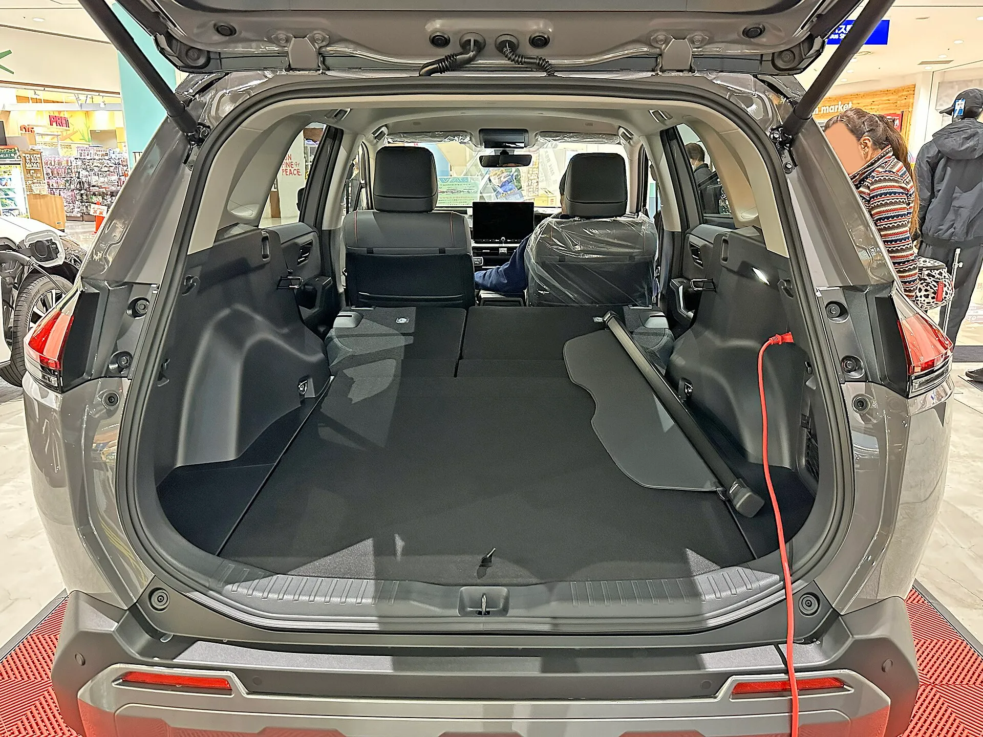 トヨタ RAV4 Adventure（ハイブリッド車・6AA-AXAN64-ANXVB）の荷室を後ろから見たところ。後席の背もたれを前に倒してあり、荷室の床が前席の背もたれの近くまで続いている。右側の内張りに赤いコードが挿さっている