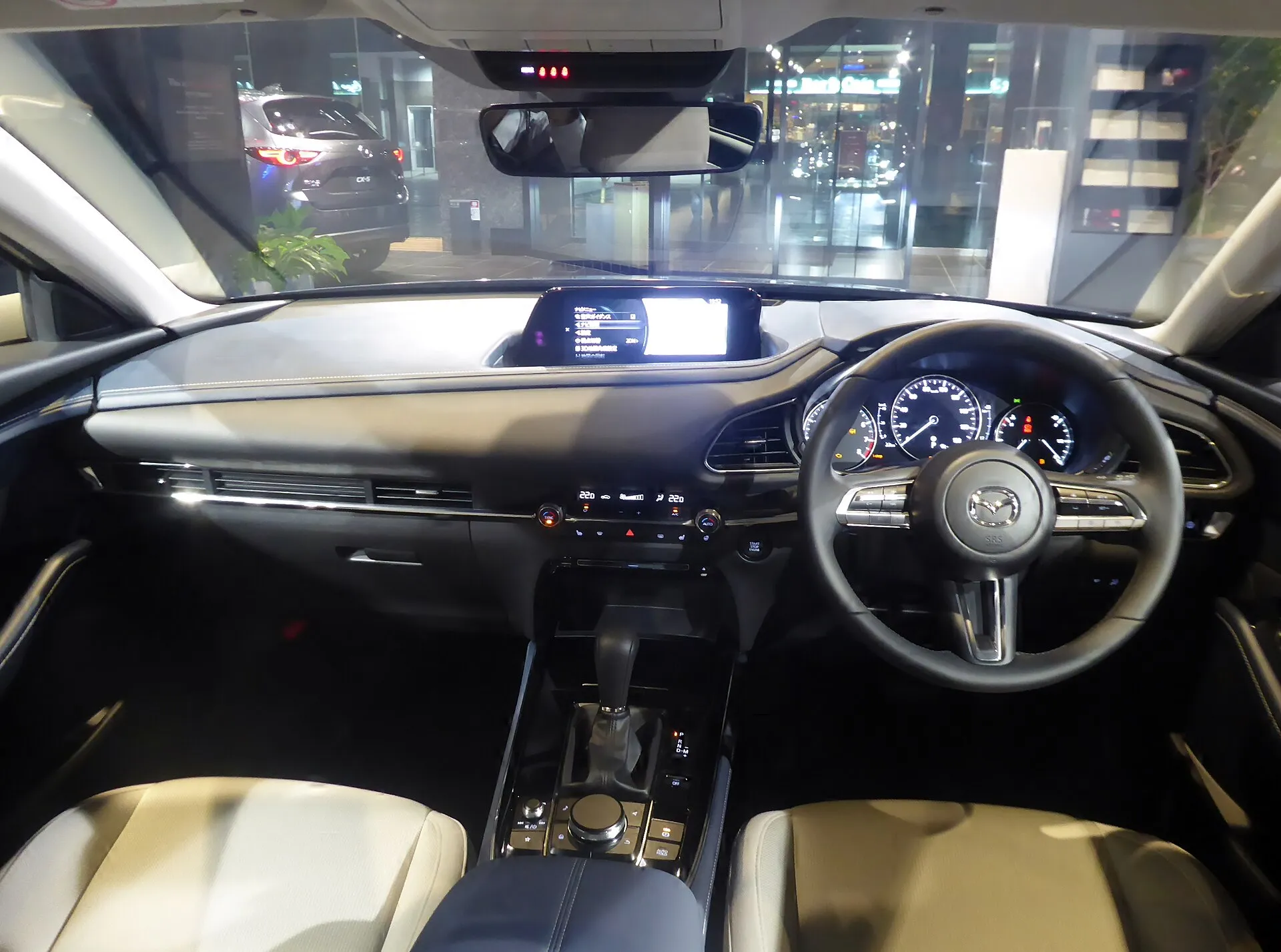 マツダ CX-30 20S L Package（2WD・5BA-DMEP）の運転席まわり。ダッシュボードの中央上部にセンターディスプレイがあり、シフトレバーの手前に丸いコマンダーコントロールがある。シートは白。2019年の個体で、グレードの名前と装備は2026年7月の商品改良後と異なる