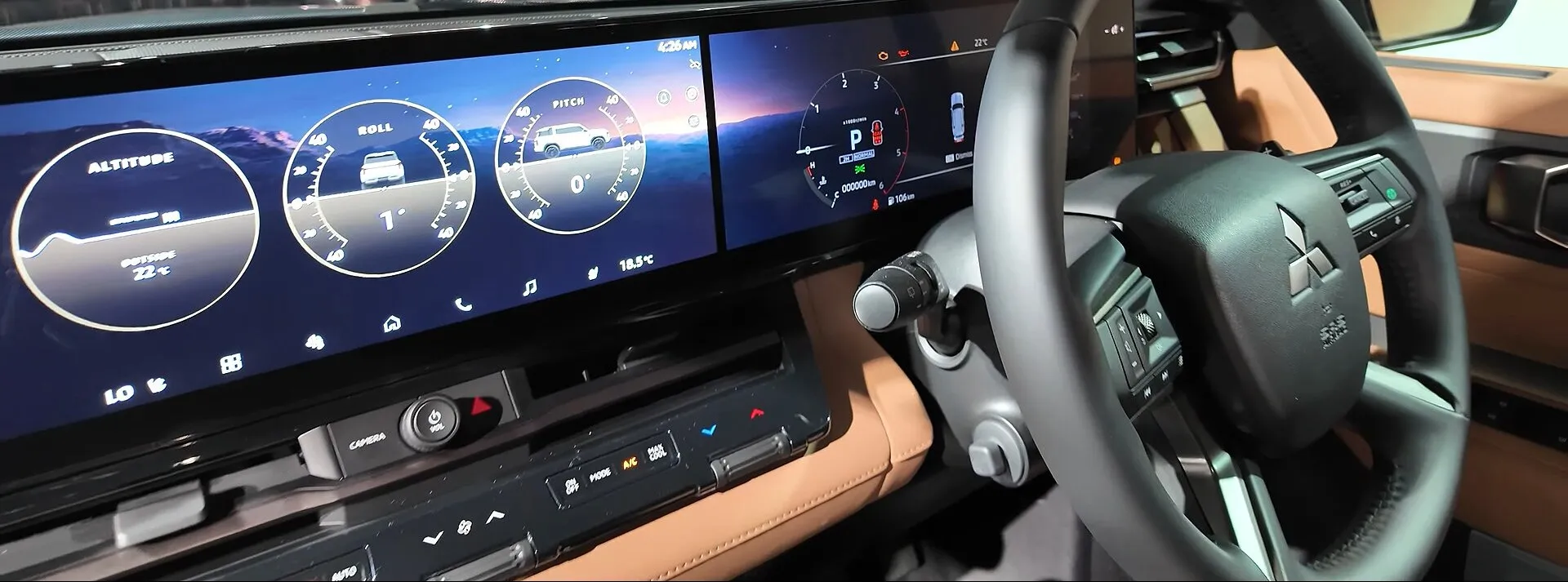 三菱 新型パジェロの運転席まわり。横に並んだ2枚のディスプレイのうち、左の画面に「ALTITUDE」「ROLL」「PITCH」と書かれた3つの丸い表示が出ていて、右の画面はメーター。右ハンドルで、内装は明るい茶色。イベントの展示車で、日本仕様かどうか、どのグレードかは写真からは分からない