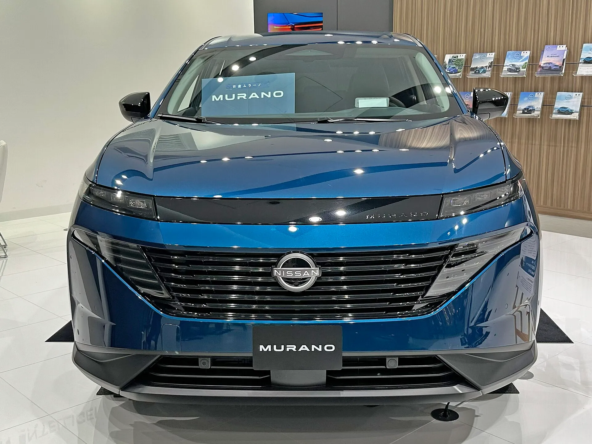 日産 ムラーノ SV(NZ53型)を正面から見た外観。青い車体の左右にドアミラーが開いた状態で張り出している。展示車で、ナンバープレートの位置に MURANO と書かれた板が付いている