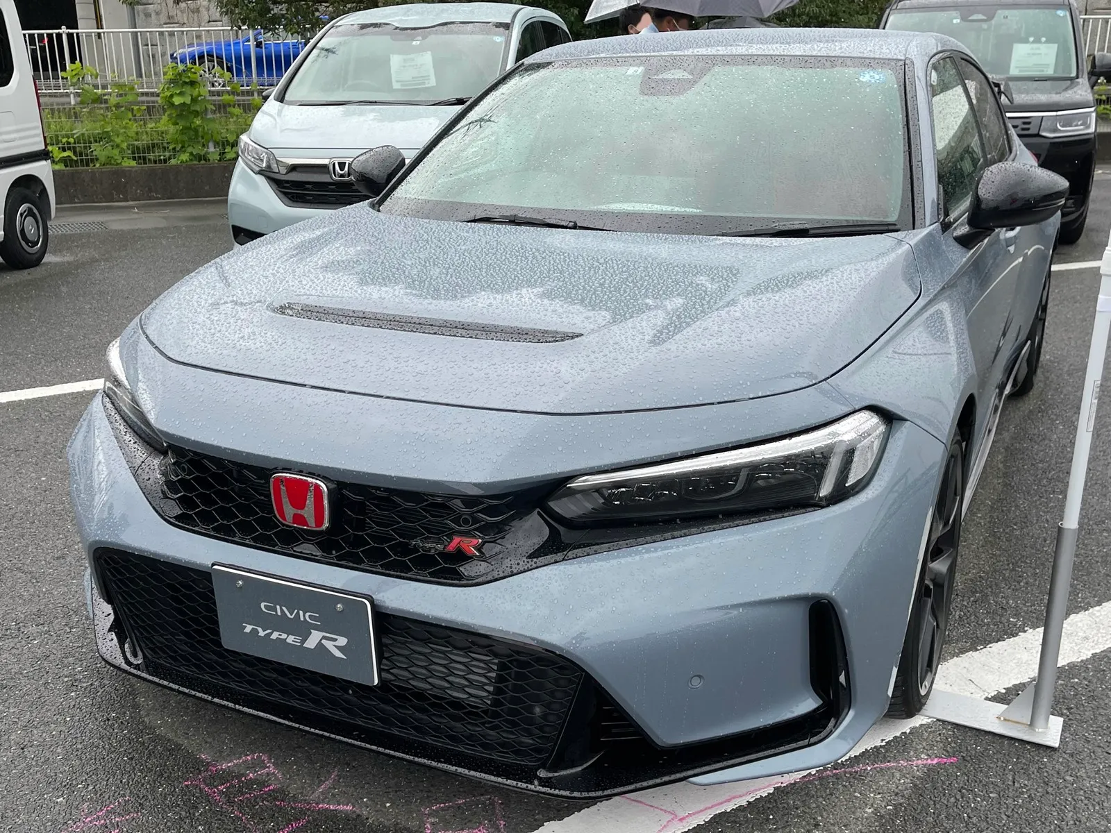 ホンダ シビック タイプR（6BA-FL5）を斜め前から見た外観。雨に濡れたグレーの車体で、ボンネットに横長の開口部があり、グリルに赤いHのエンブレム、ナンバーの位置に「CIVIC TYPE R」のプレートが付く